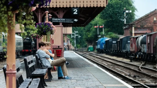 Two young people sat on a bench at an idyllic-looking train station