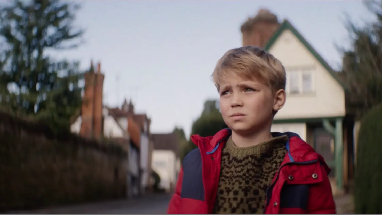 A young blonde boy standing on a street with a pensive, apprehensive look