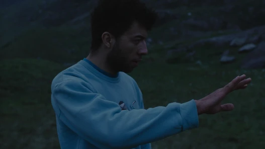 Dusk, a young mixed-raced man lifts his hand.