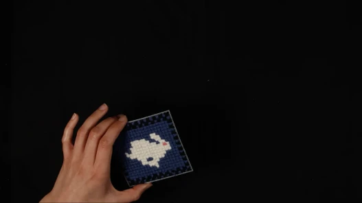 a hand holding a cross stitch square with a rabbit