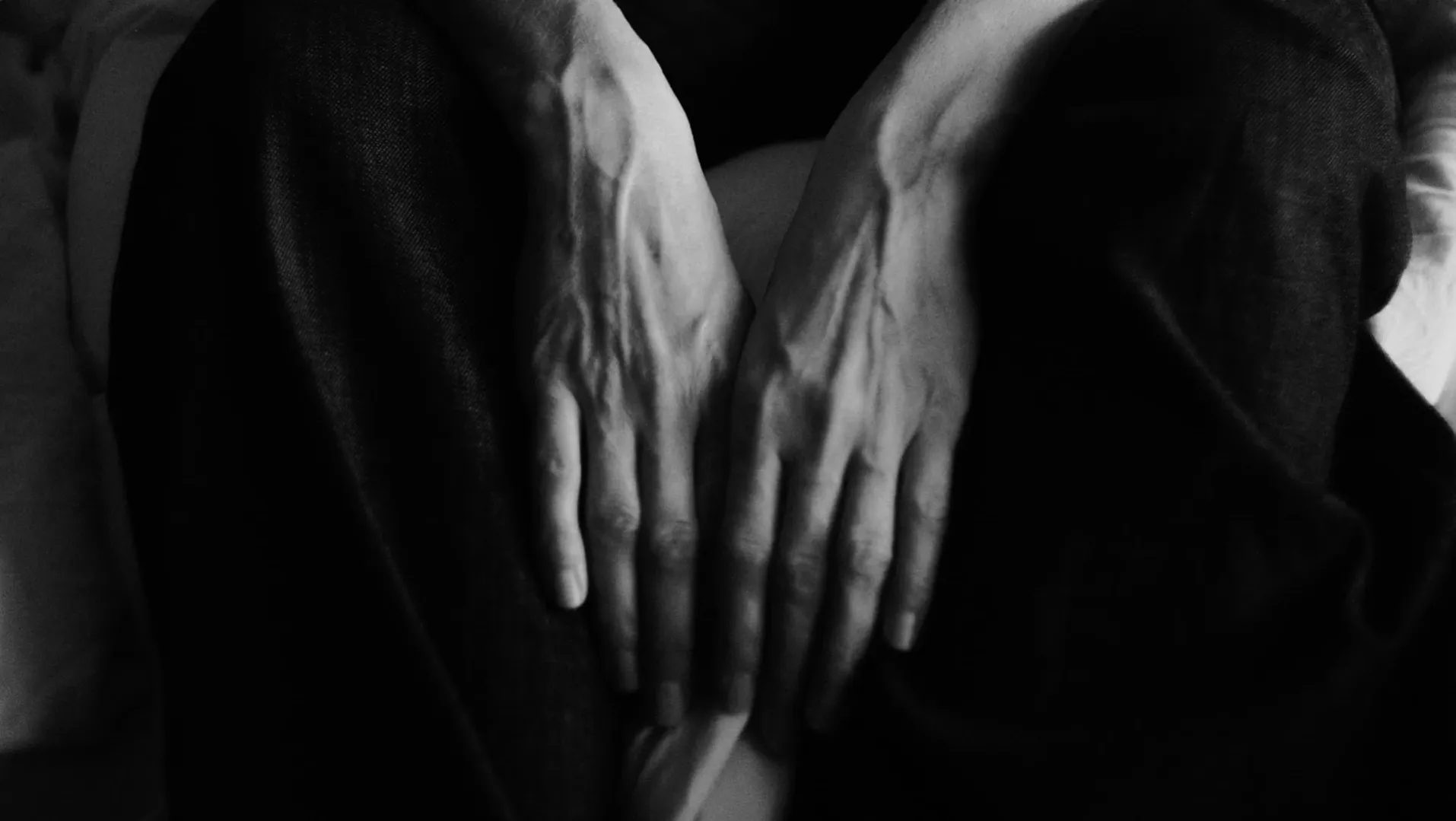 A woman sits on bed, we see her hands between her knees