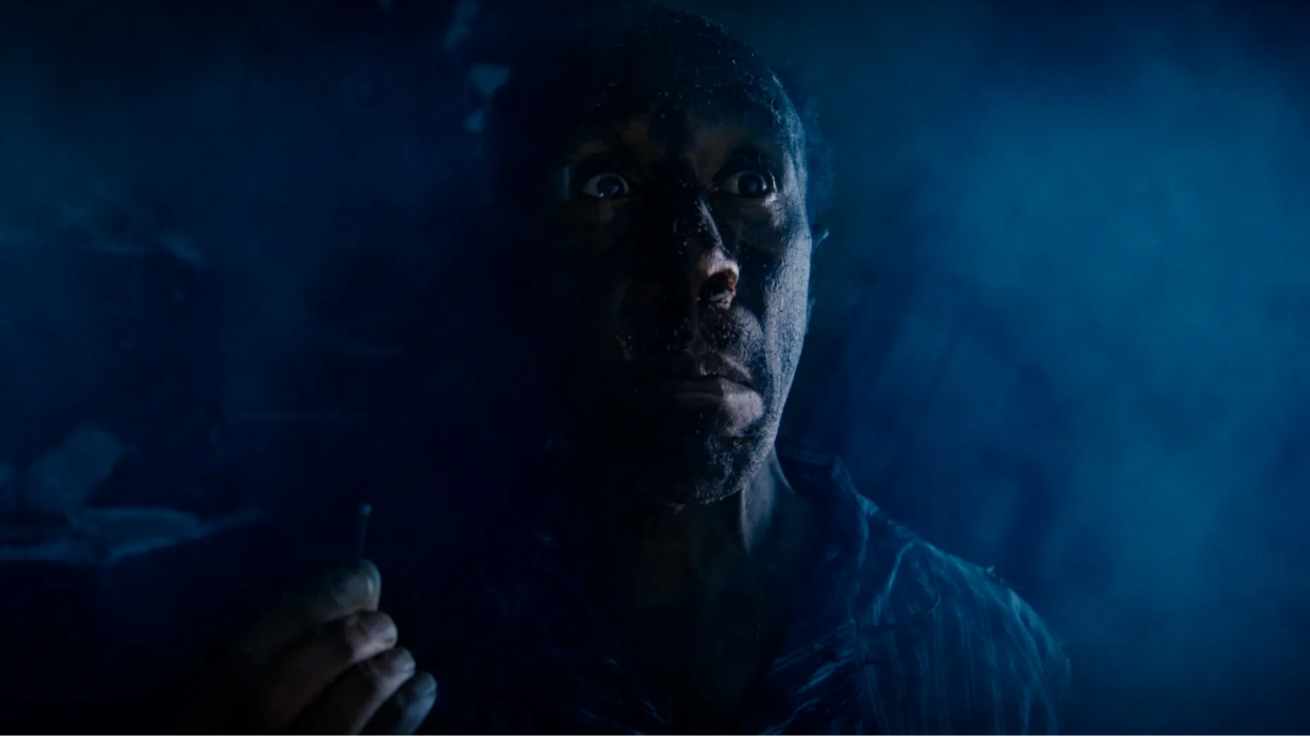 Danny John-Jules in Sound Asleep. A man holds a burned match in a smoke filled room, with a surprised look on his face.