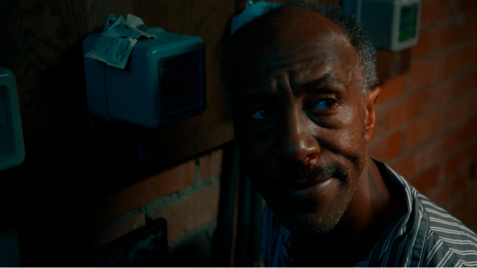 Danny John-Jules in Sound Asleep. A man in pyjamas in the brick basement next to electricity meters.