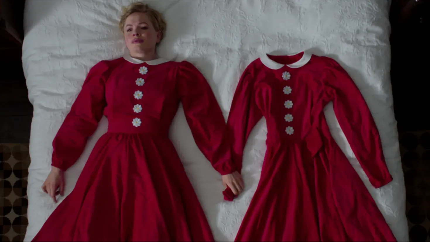 A woman in a vintage look red dress lies on a bed holding onto the arm of a replica red dress.