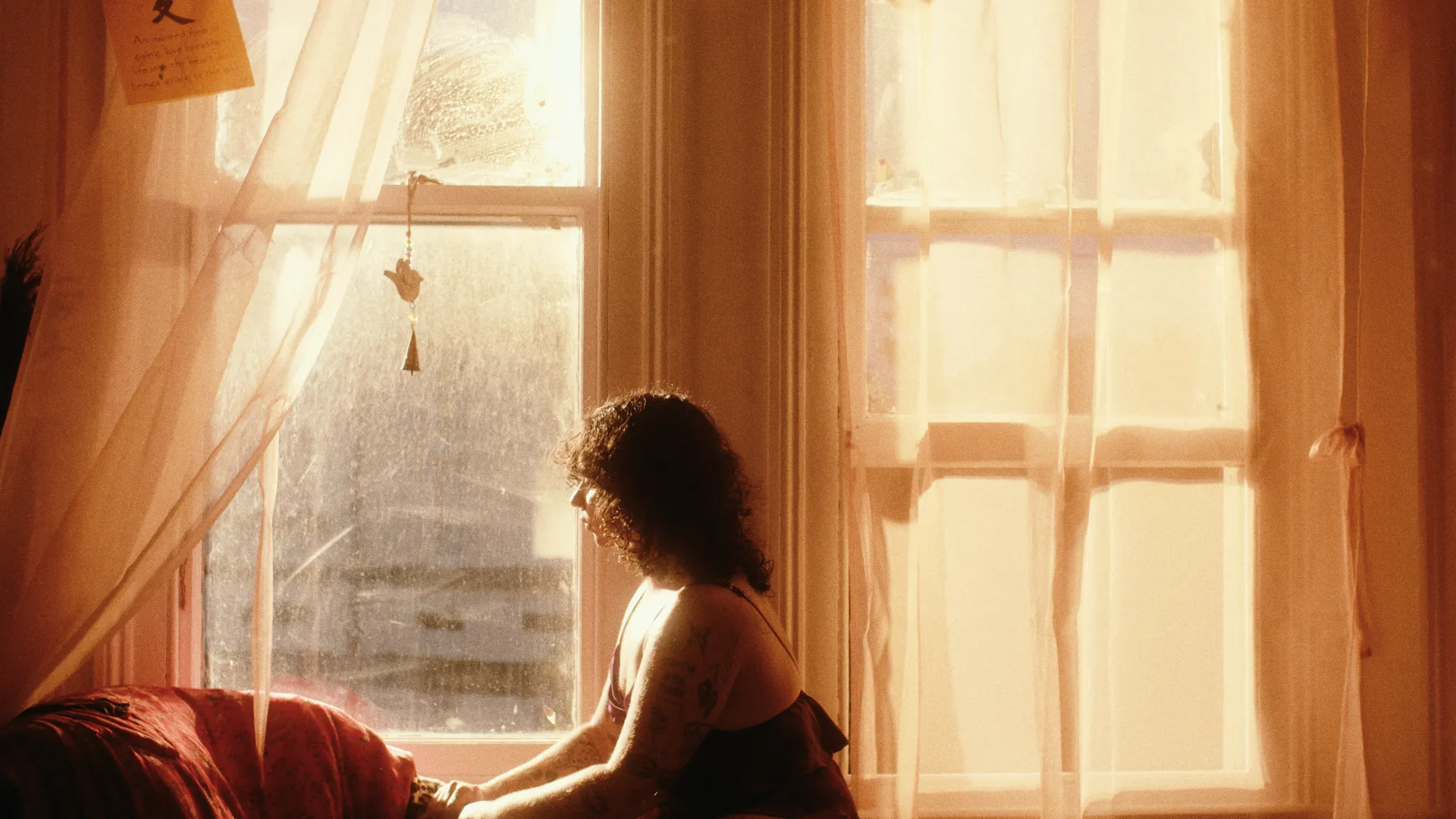 A person sitting next to a window, looking out of it. The room is bathed in warm, morning light.