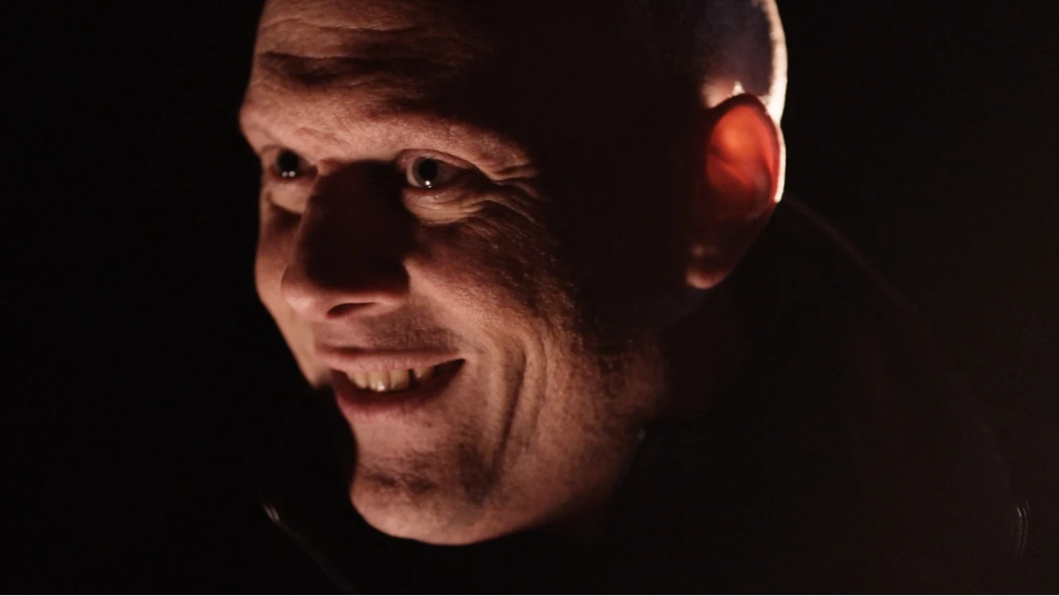 A man grinning menacingly illuminated by car headlights