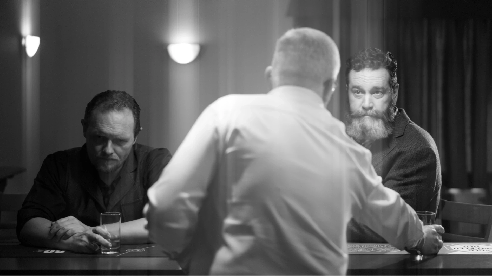 Three men at a bar, one being served a drink. The image is in black and white with a slight haze to evoke the idea that this is a memory from the past