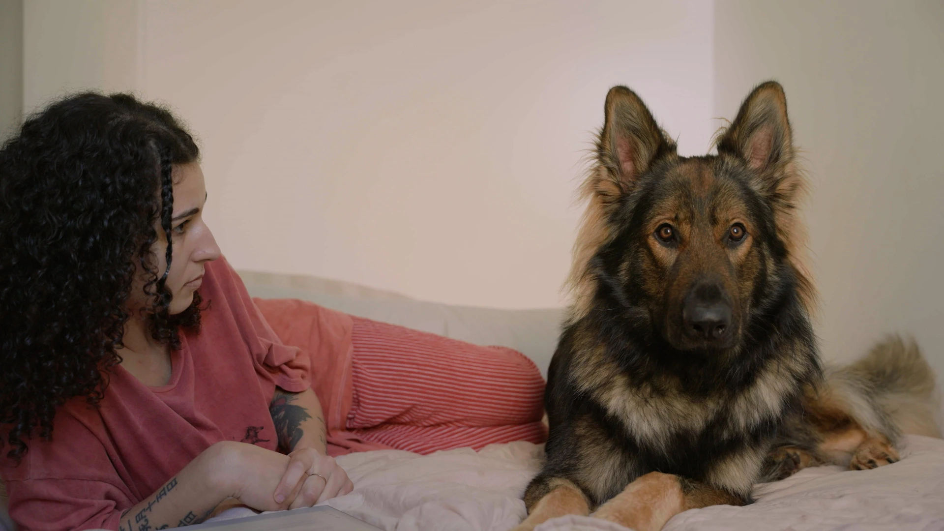 A woman and her German Shepherd dog sit on a bed