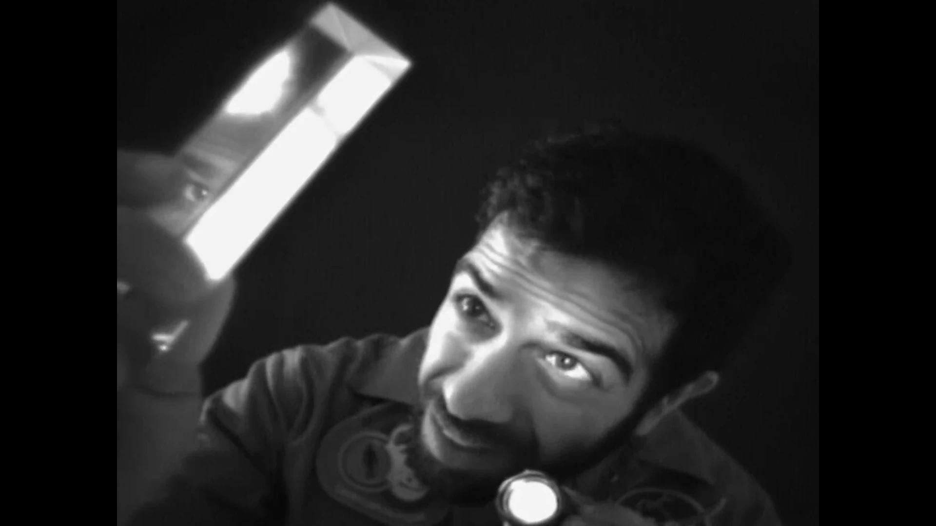 Black and white close up of a man holding a torch up to a prism in front of face, in it his eyes are reflected