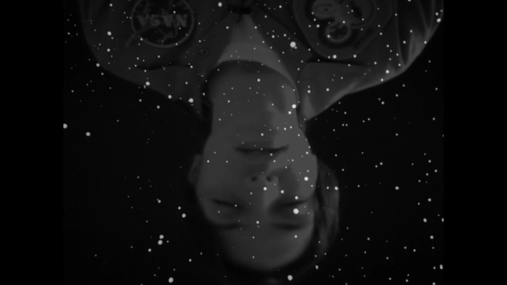 Black and white close up of a woman upside down with eyes closed, surrounding her are a field of stars