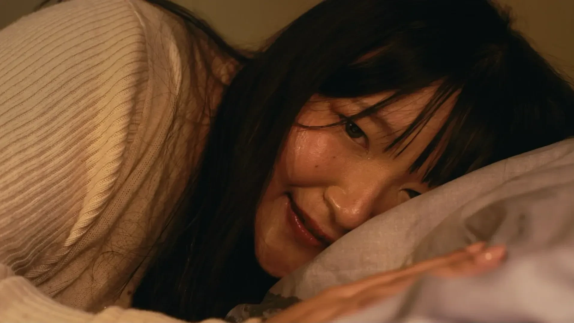 A woman laying on a bed smiles eerily.