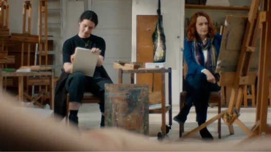 Two women sitting side-by-side in an art class among easels and drawing boards
