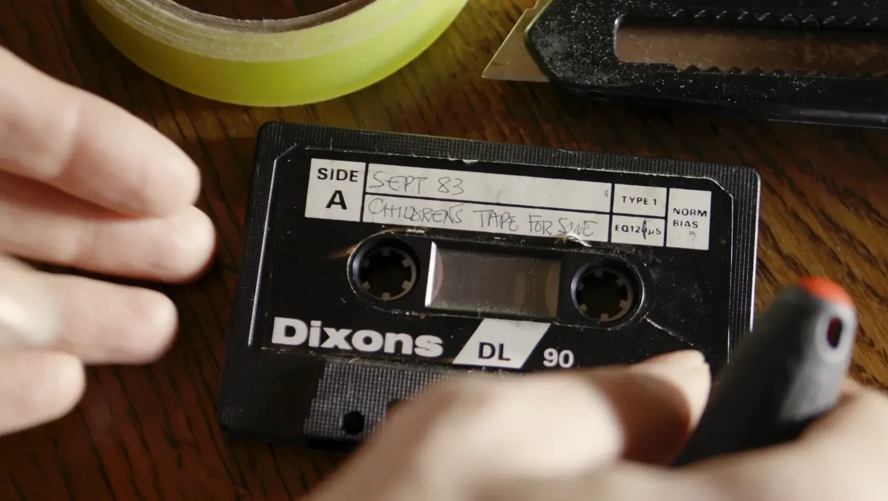 An audio cassette tape, with the title 'Childrens Tape for Sue', being repaired.