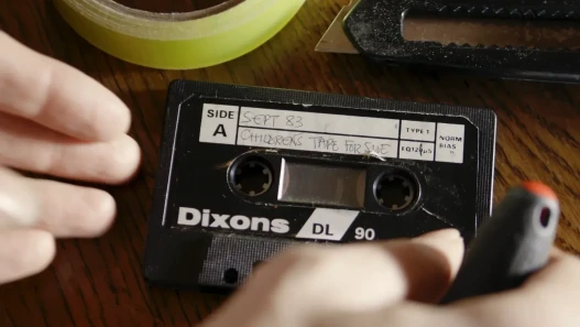 An audio cassette tape, with the title 'Childrens Tape for Sue', being repaired.