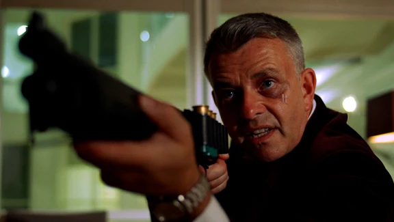 Middle-aged man with well-groomed grey hair aims a shotgun in a tense pose, a bruise around one eye, set against a gritty urban background, framed as a cinematic still.