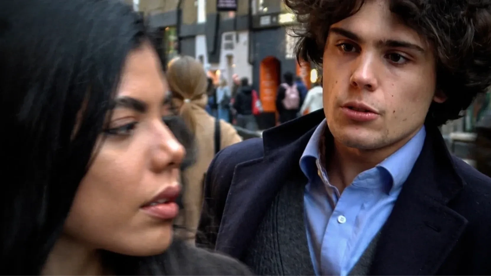 In a busy street, a young man, attempts to catch the attention of a young woman.