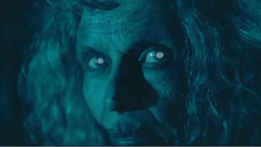 An elderly woman with glowing eyes looks past the camera.