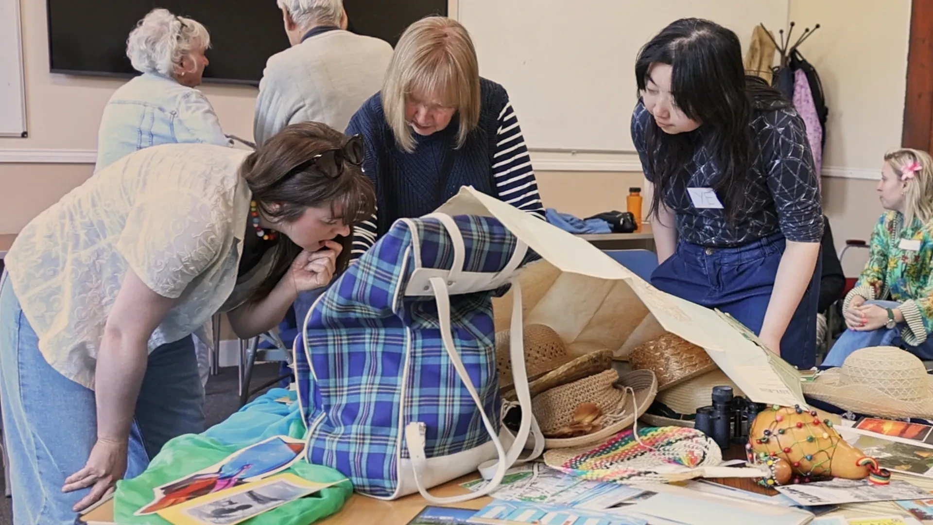 Three women look at a map on a table of travel-themed objects.
