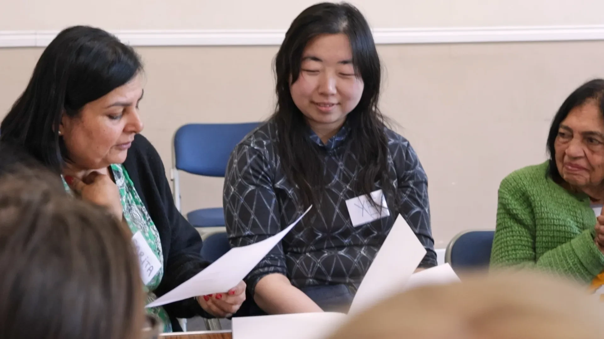 One woman reads from a paper, while a younger woman and and older woman sat next to her smile.