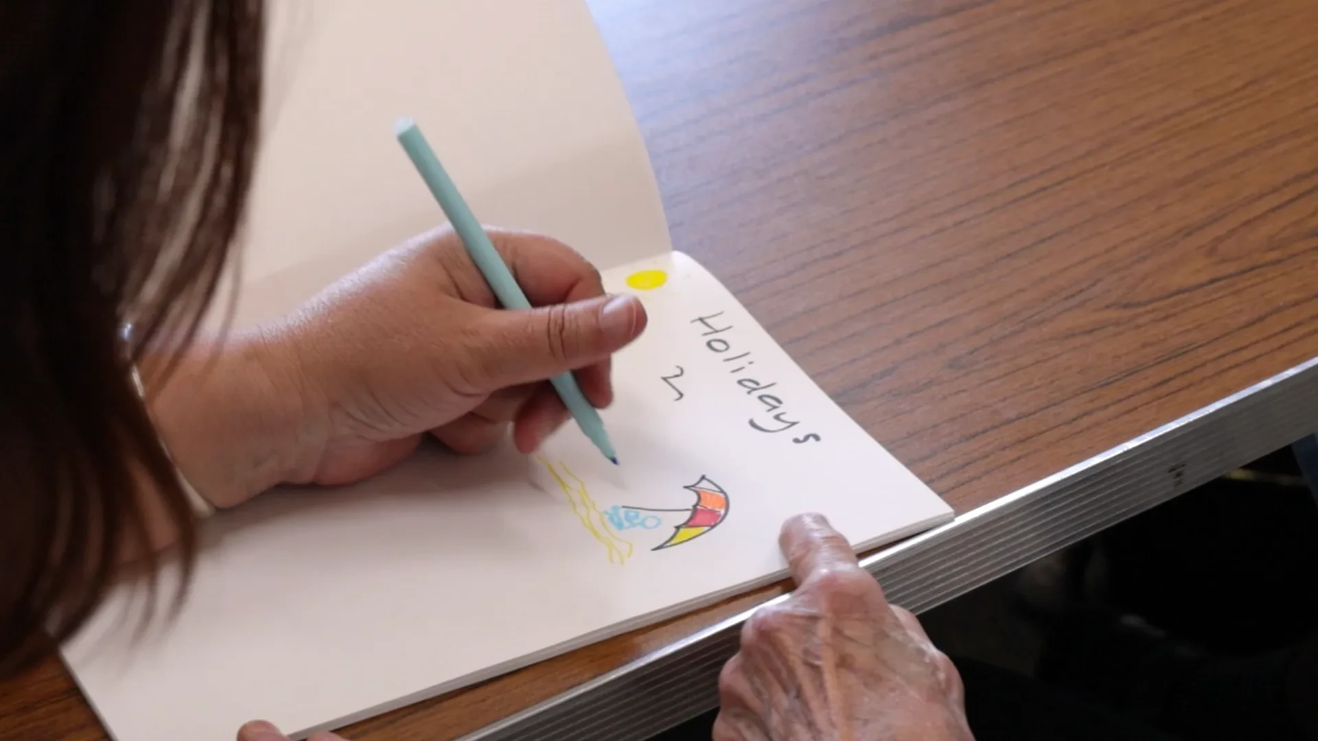A person is drawing a beach umbrella in a sketchbook.