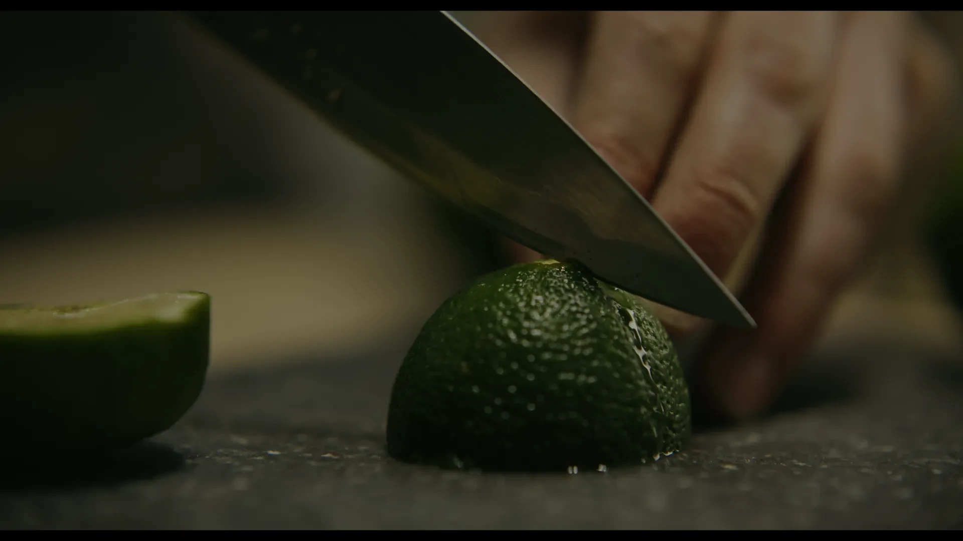 A knife cuts into a lime, juice running down the side