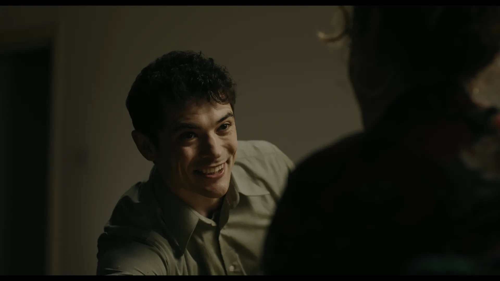 A dark haired man leans forward, smiing
