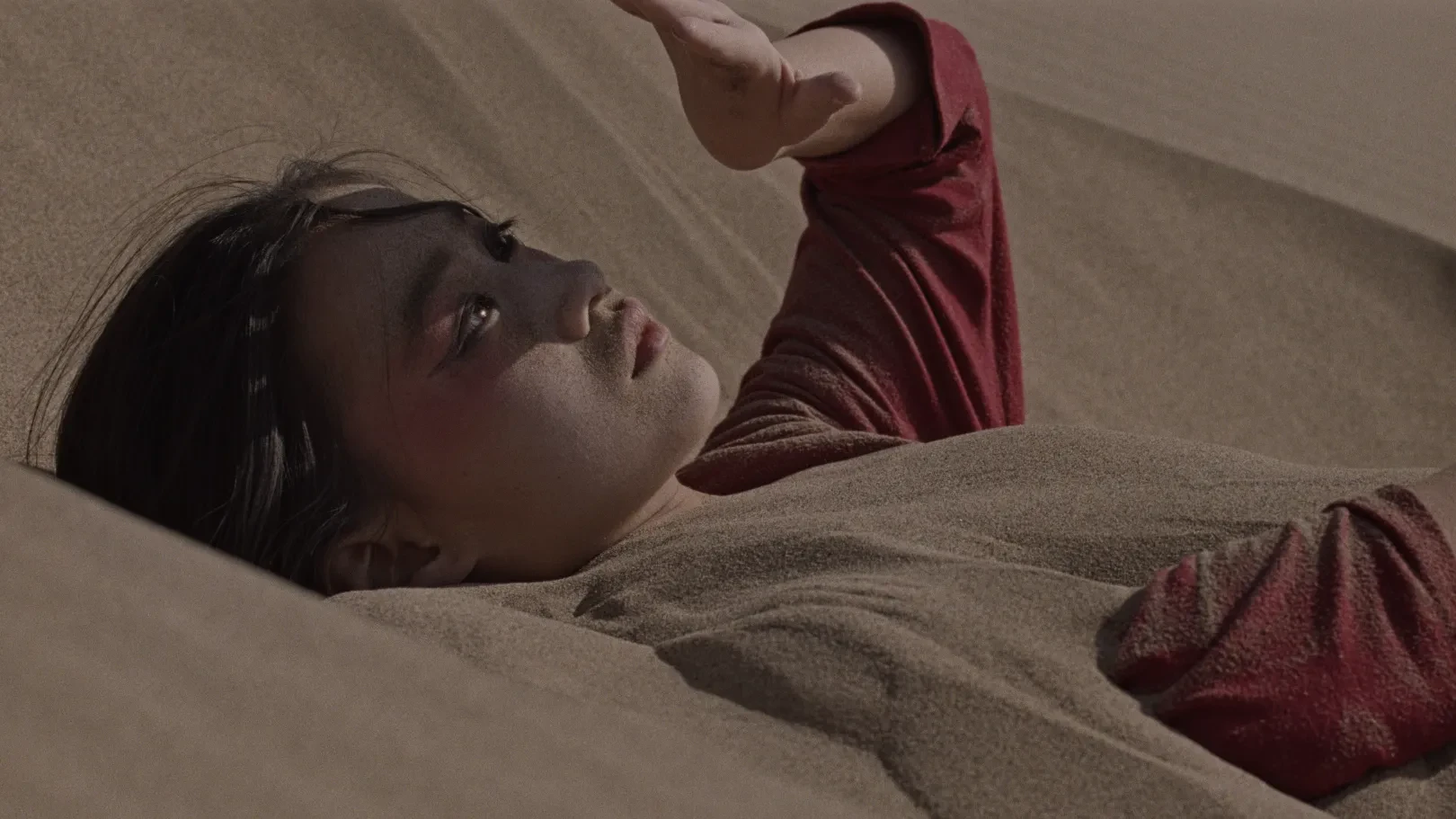 A girl lies in the desert partially covered in sand