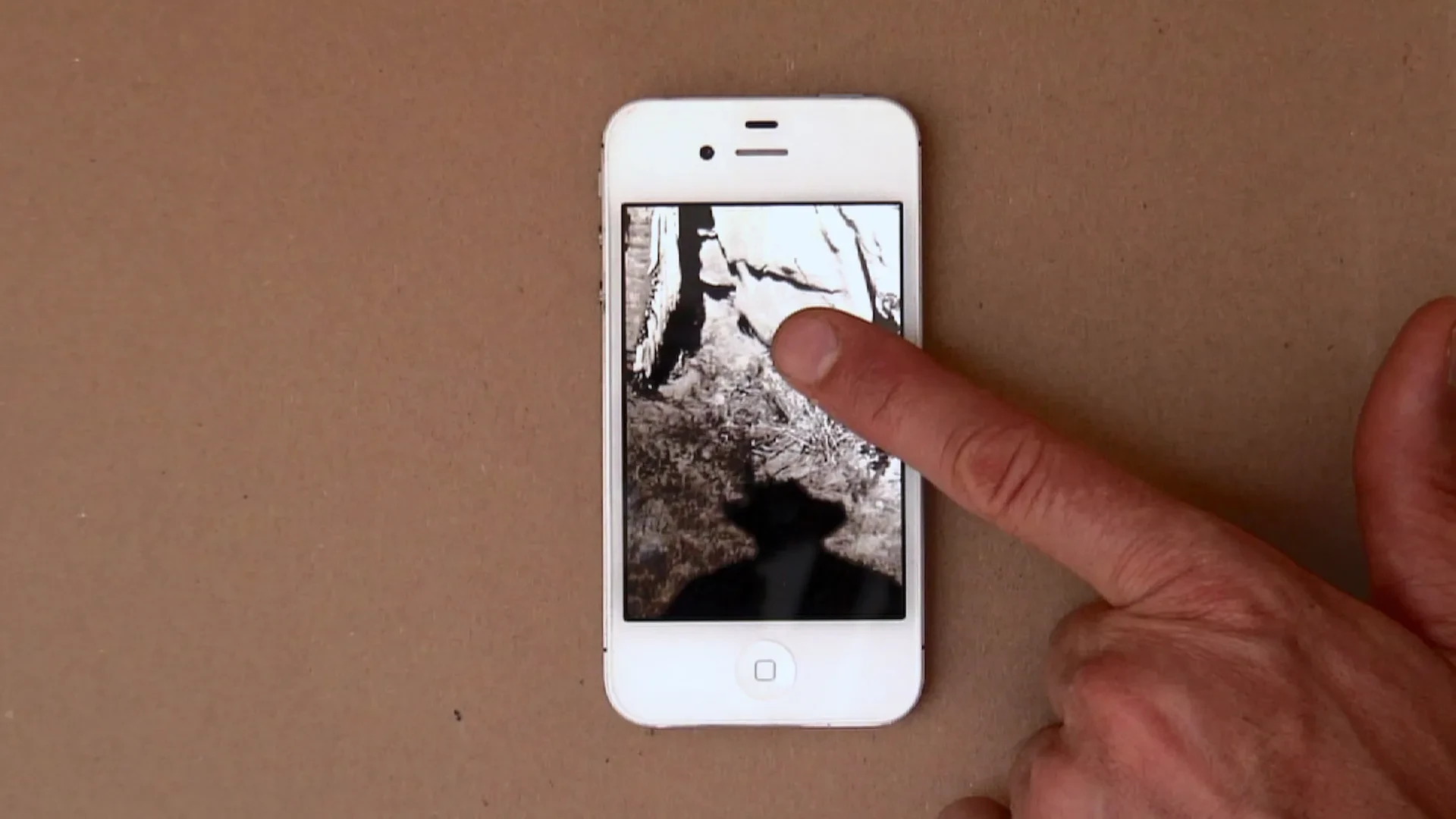 A finger touching an iPhone screen with a b/w photograph shown.