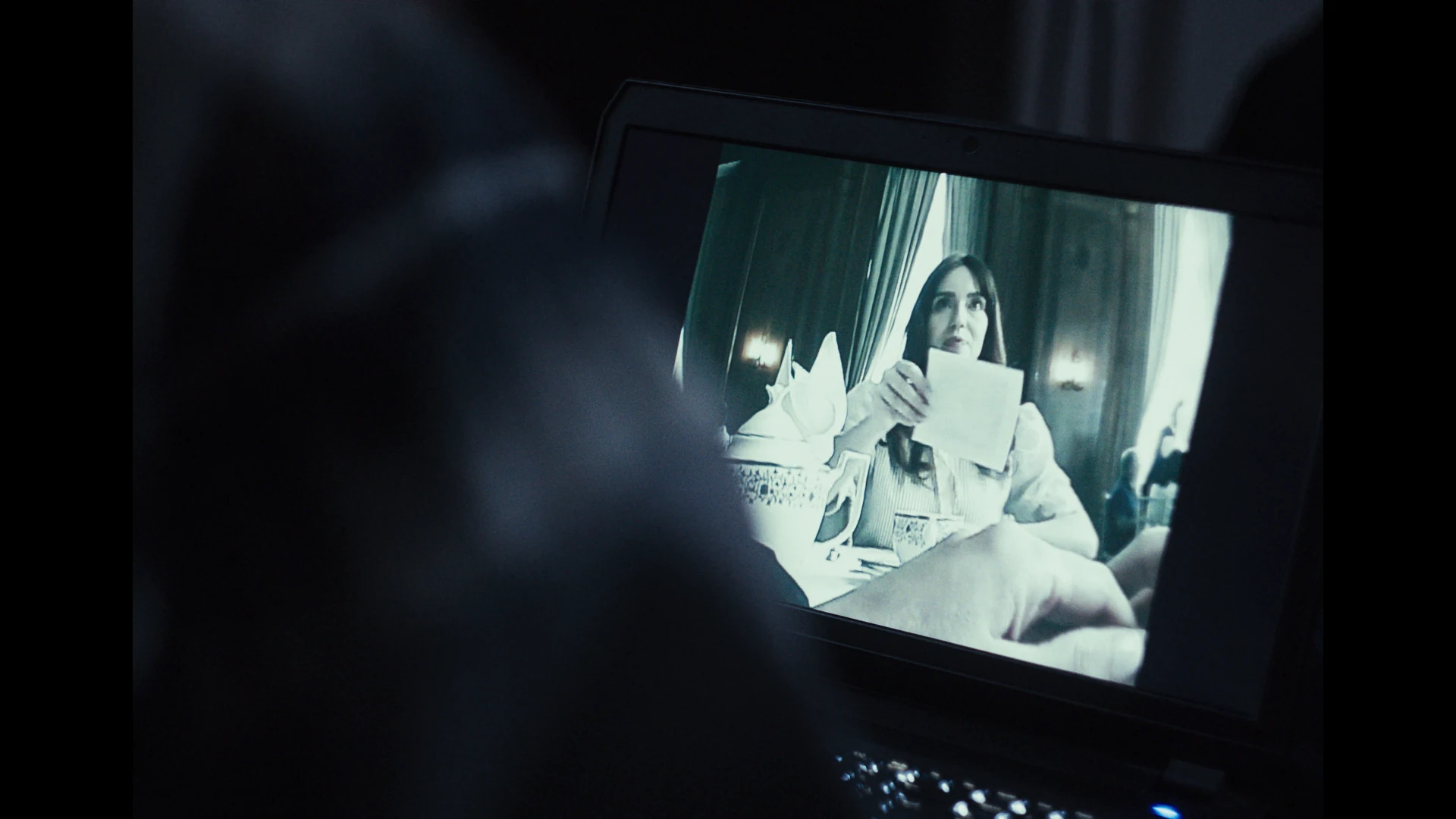A laptop recording of a woman sitting at a table holding a piece of paper 
