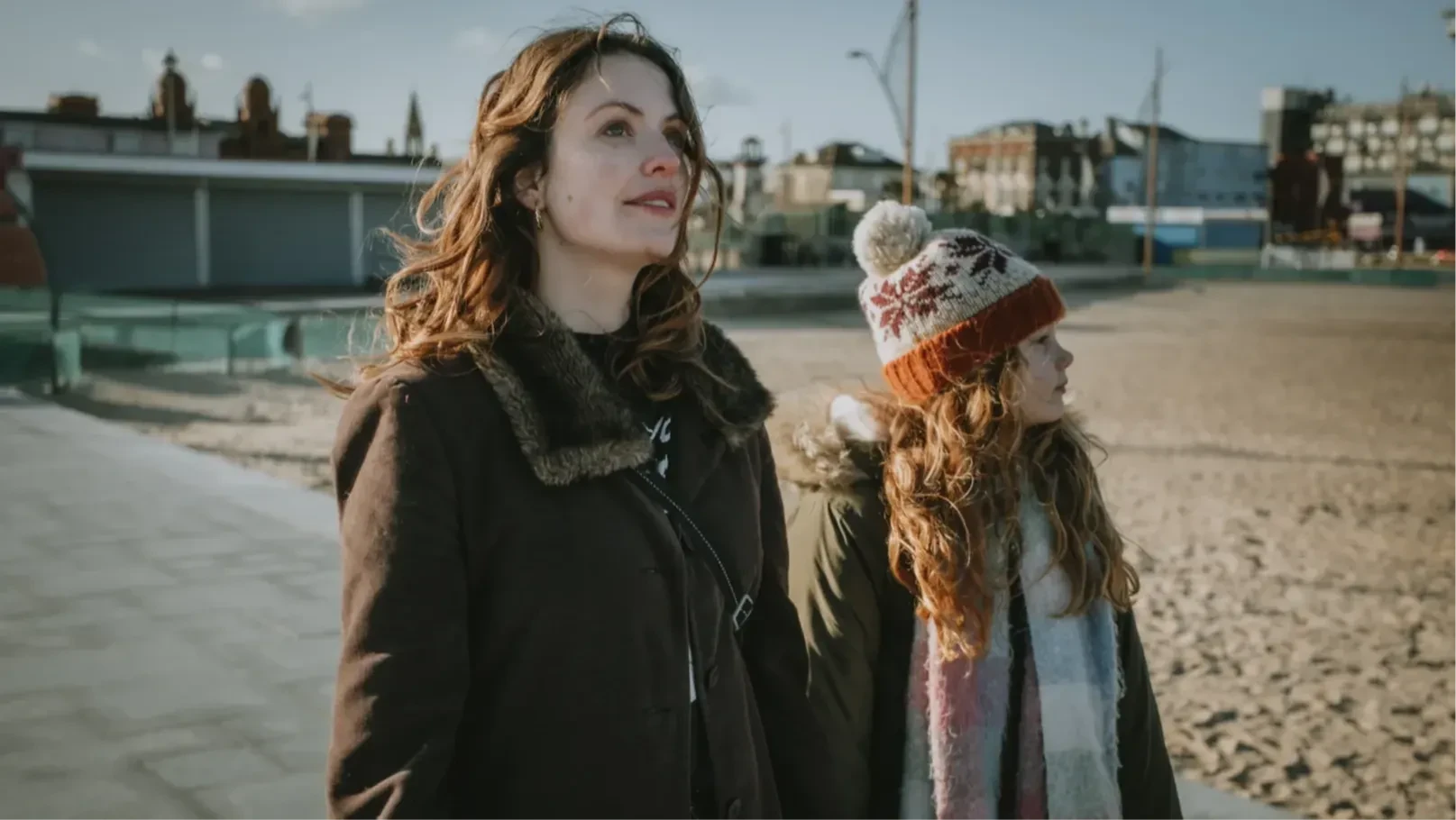 A woman and a girl walk at the side of a beach.