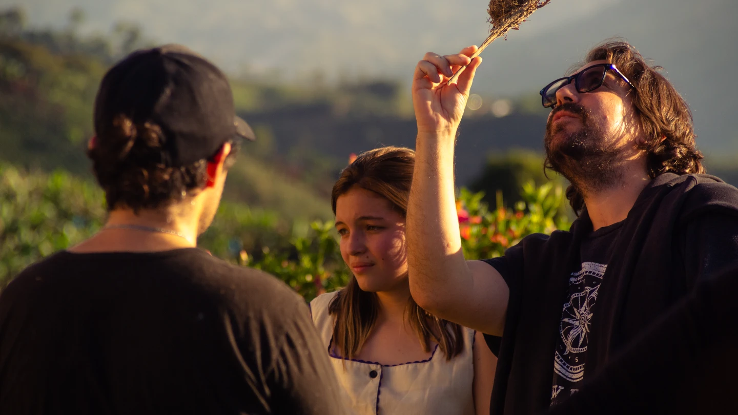 Two men and a woman in green surroundings. One man inspects a small branch in the sunlight.
