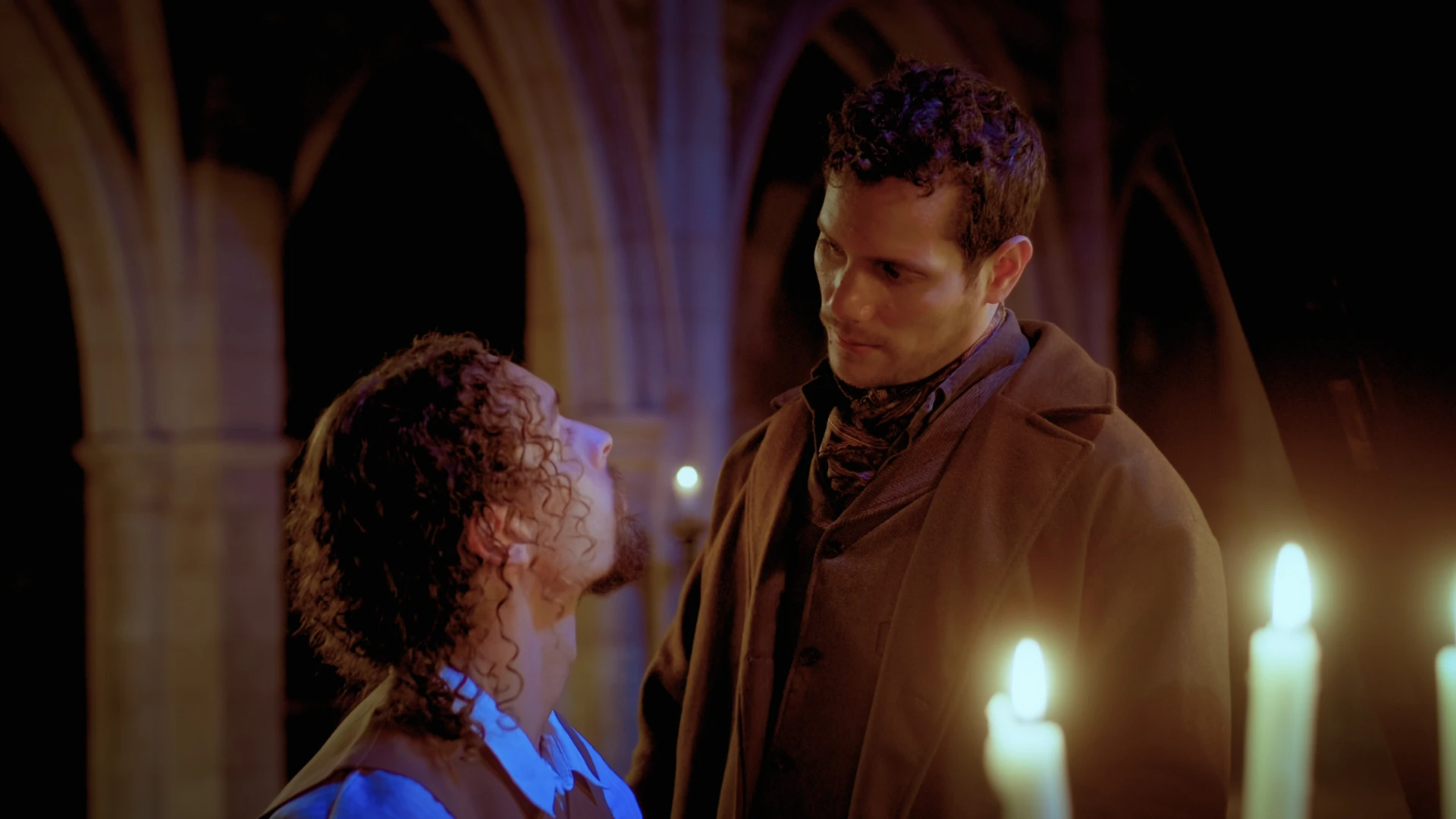Both of the Male Leads looking into each other's eyes by the piano. Candles in foreground.
