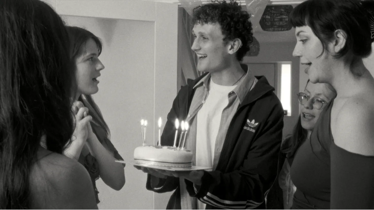 A  black and white image of a group of teenagers with a birthday cake.
