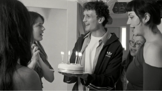 A  black and white image of a group of teenagers with a birthday cake.