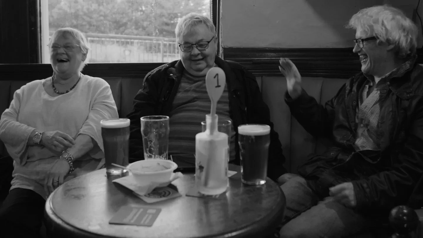 Three people sit around a table with pints