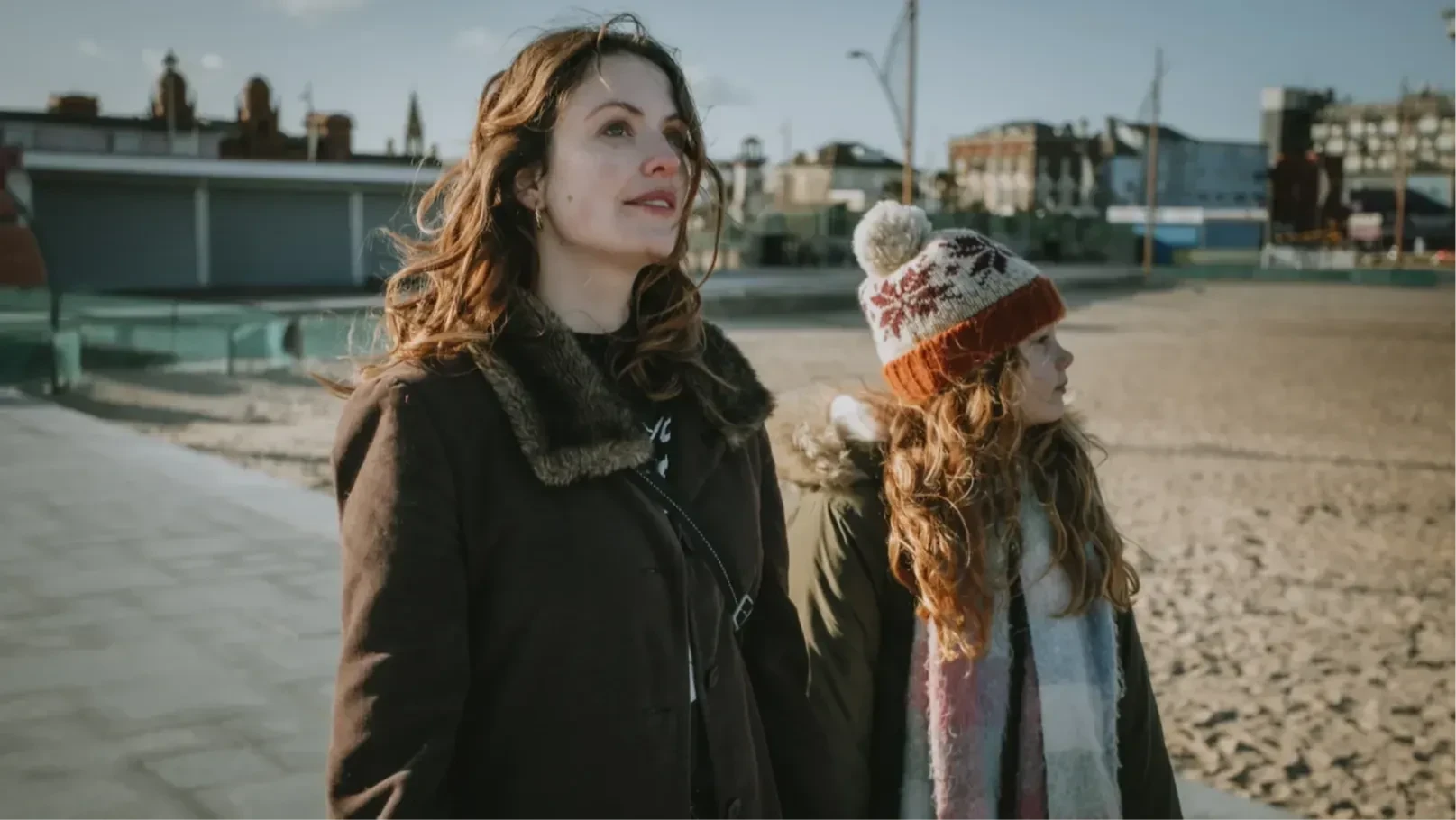 A woman and a girl walk at the side of a beach.
