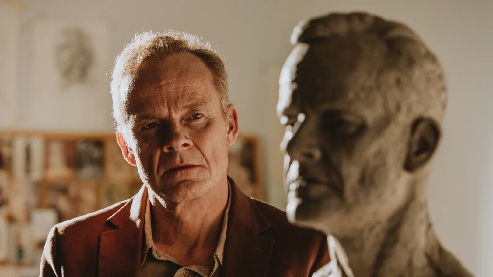 Man looking at a sculpt of a male figure in a warmly lit room.