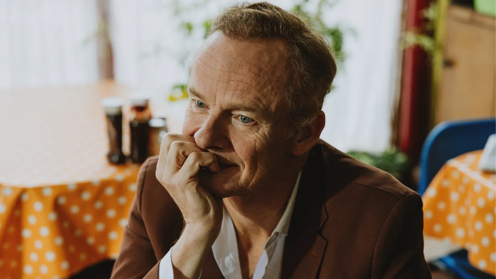 Man resting his hand against his face shielding a small smile, seated in a cafe.