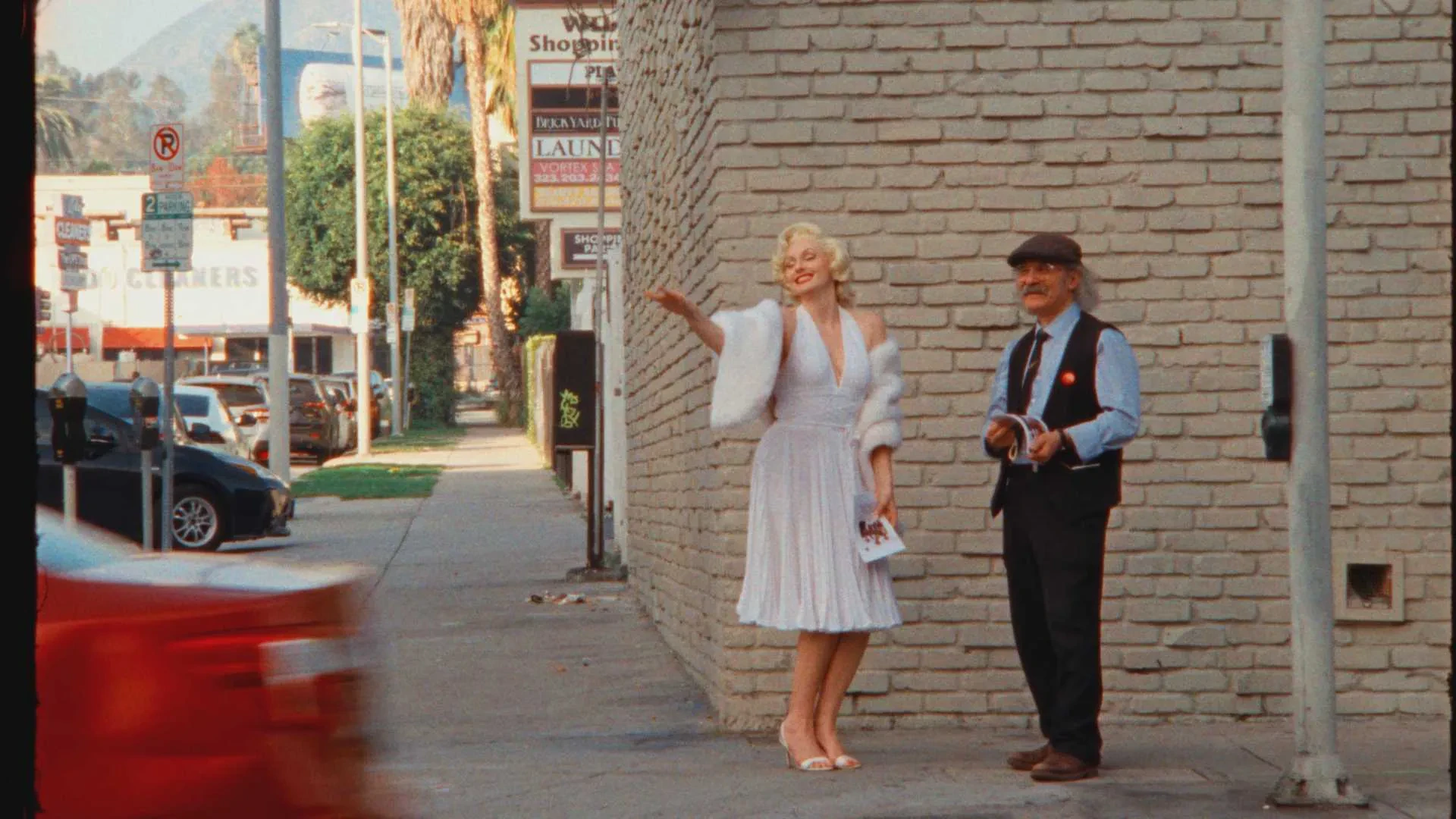 A Marilyn Monroe impersonator in a white dress and Umit Mesut standing on a Los Angeles street as cars pass.
