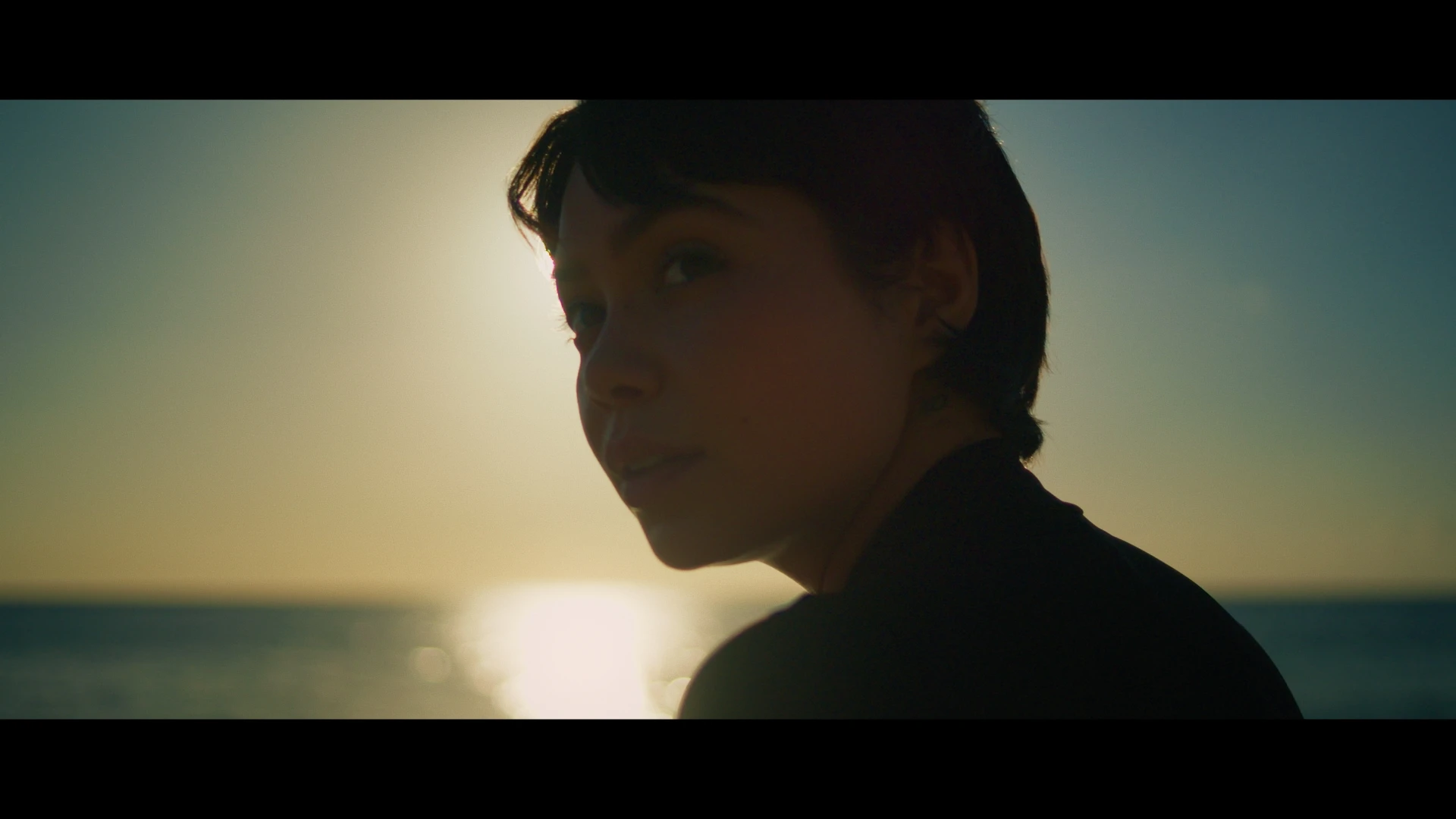 A woman looks over her shoulder behind her with the ocean in front of her