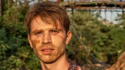 A muddied dishevelled man looks into the camera