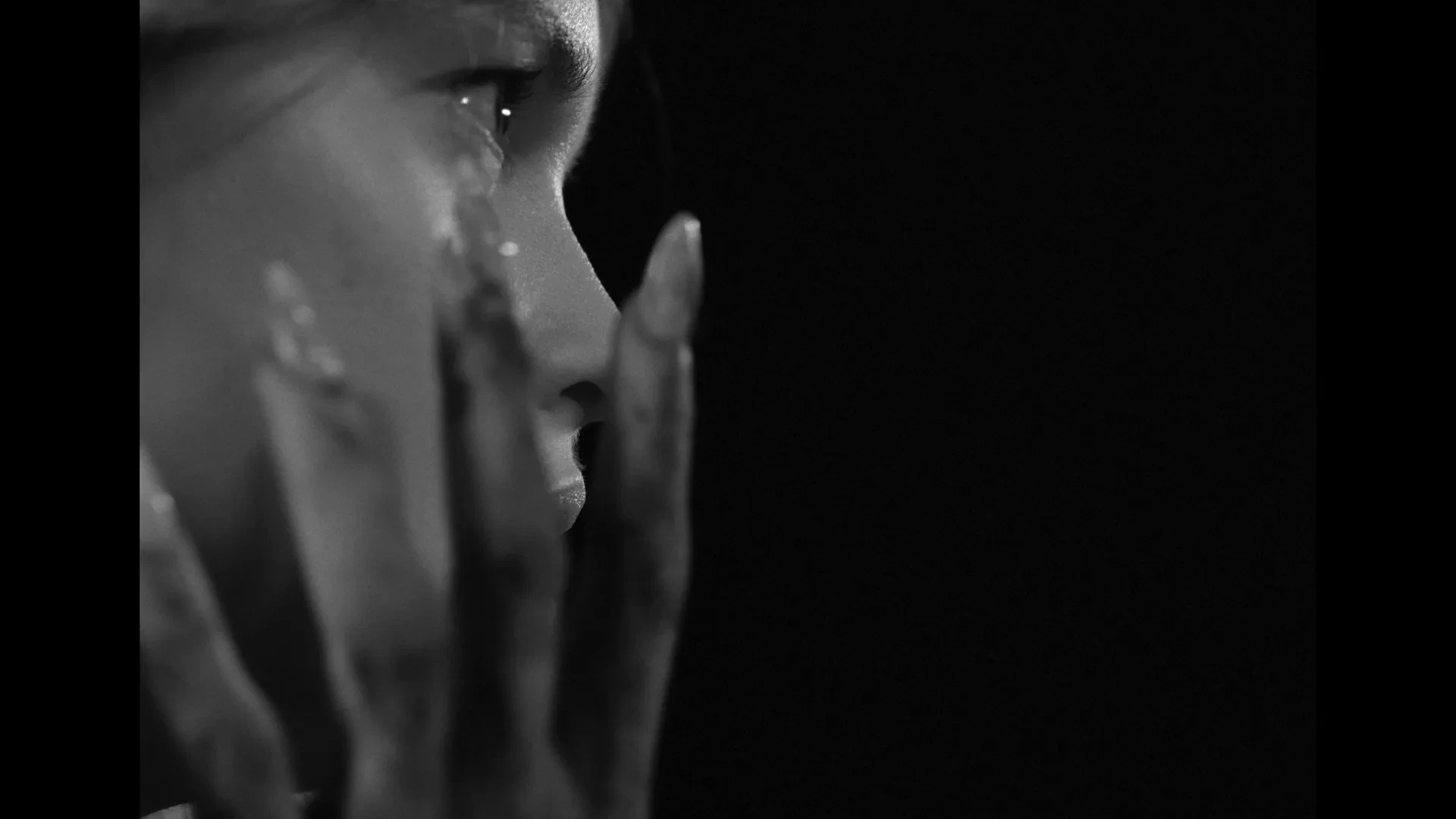 A black and white image of a woman's face being grabbed by a long-nailed hand