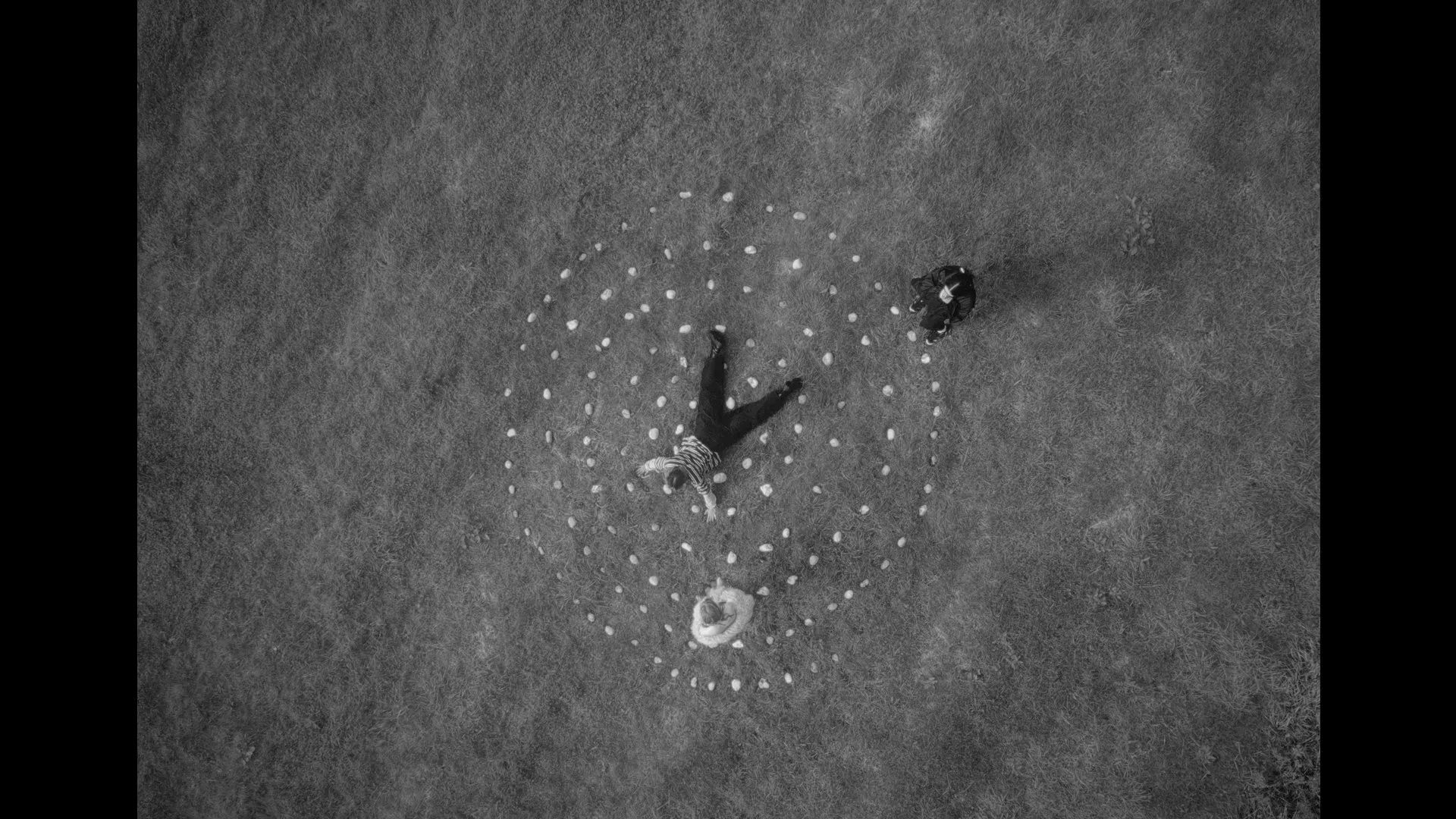 A black and white aerial shot of a stone formation of a spiral, three figures stand within it