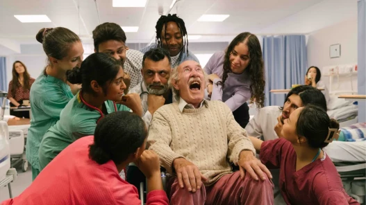 A man in a hospital chair sings surrounded by patients and hospital staff