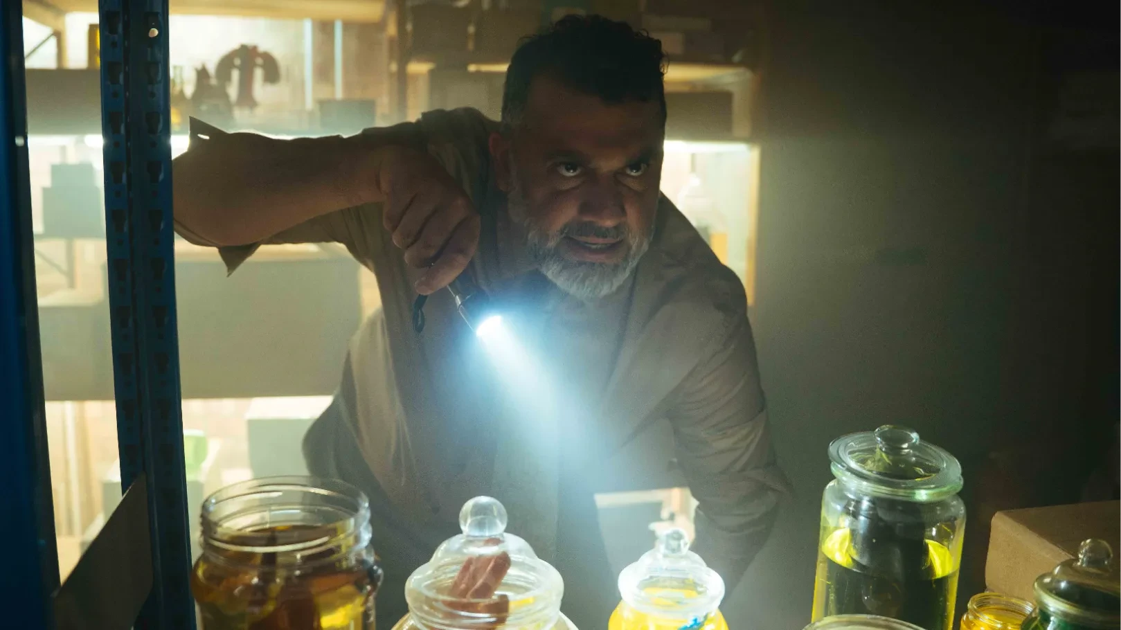 A man (Irvine Iqbal) shines a torch in the room of foreign objects