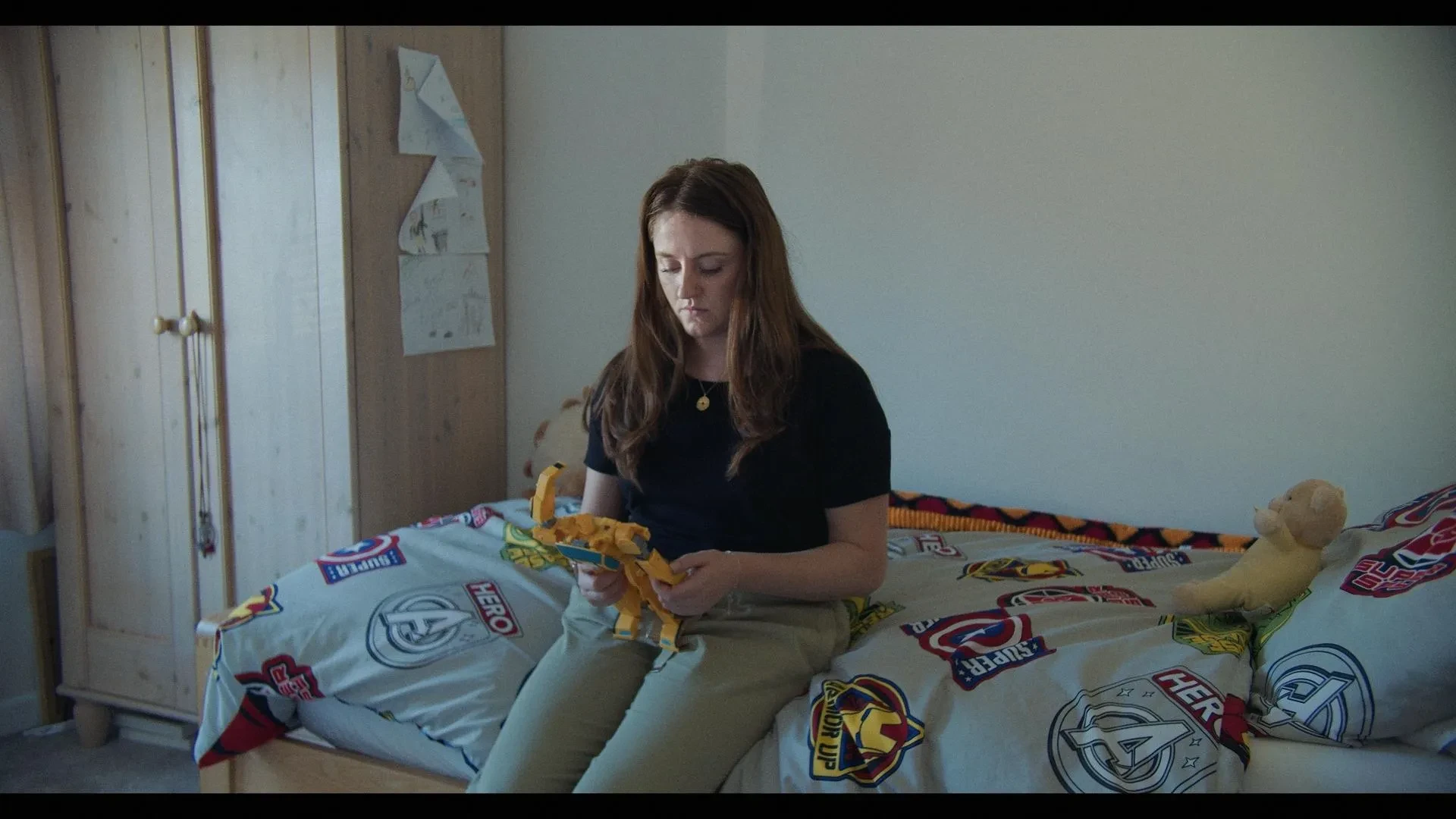 Samantha (played by Portia Crewe) sits on her late sons bed holding one of his toys, a yellow robot.