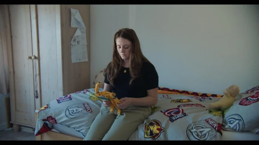 Samantha (played by Portia Crewe) sits on her late sons bed holding one of his toys, a yellow robot.