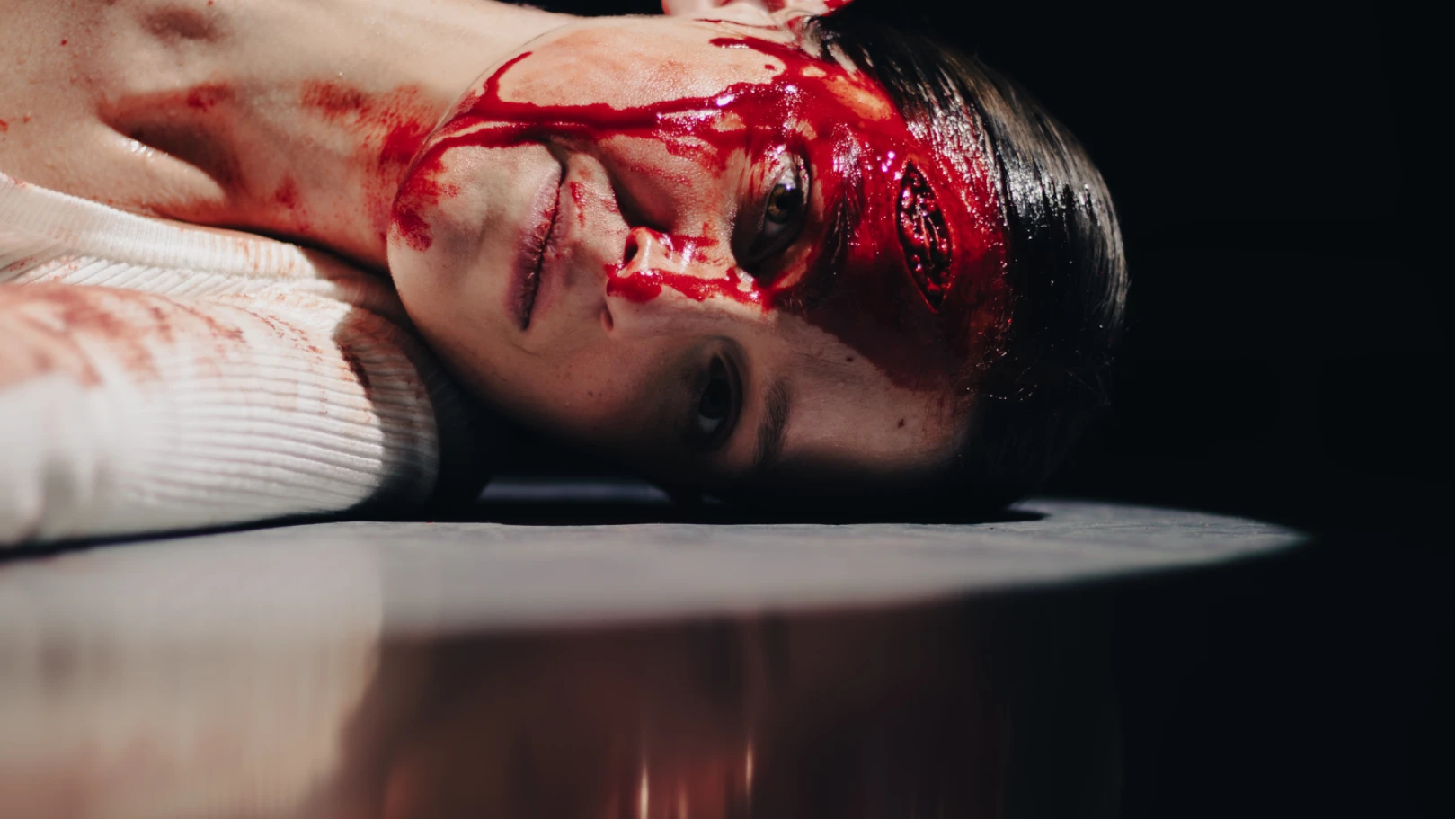 A woman lays on the ground with a bleeding head wound. 