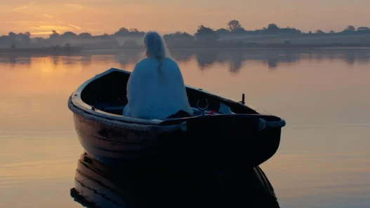 A woman in a boat on water in the warm glow of dawn