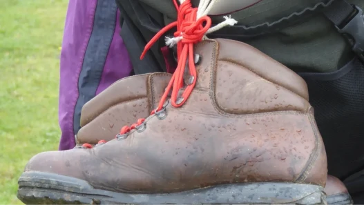 A pair of brown walking boots with red laces, tied to the back of a rucksack.